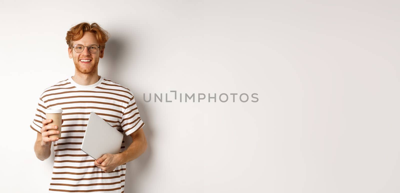 Handsome redhead male employee in glasses having break, drinking coffee and holding laptop, standing over white background by Benzoix