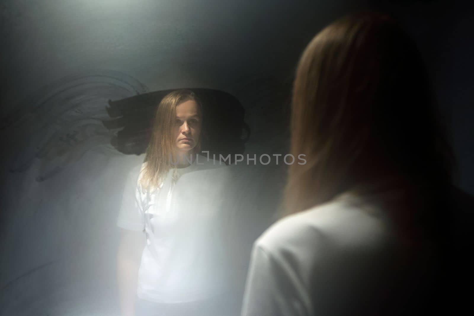 Blond woman in the reflection of sweaty mirror. Female in white t-shirt staring at herself with blank look. Age crisis