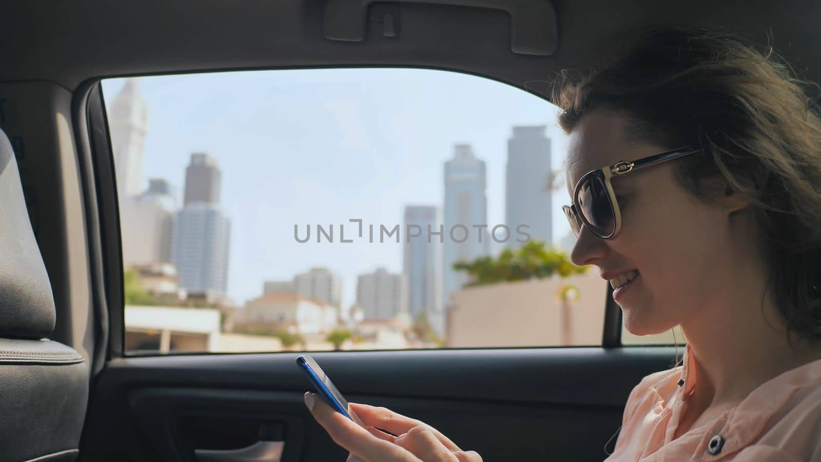 A girl in a moving car is typing a message on the phone. Dubai city. by DovidPro