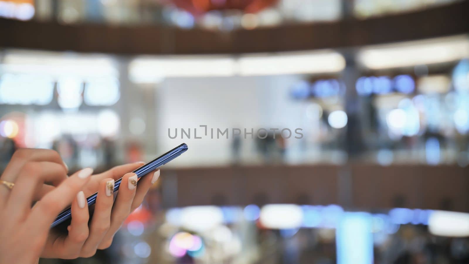 A girl in a shopping mall dials a message on the phone. Hands close up