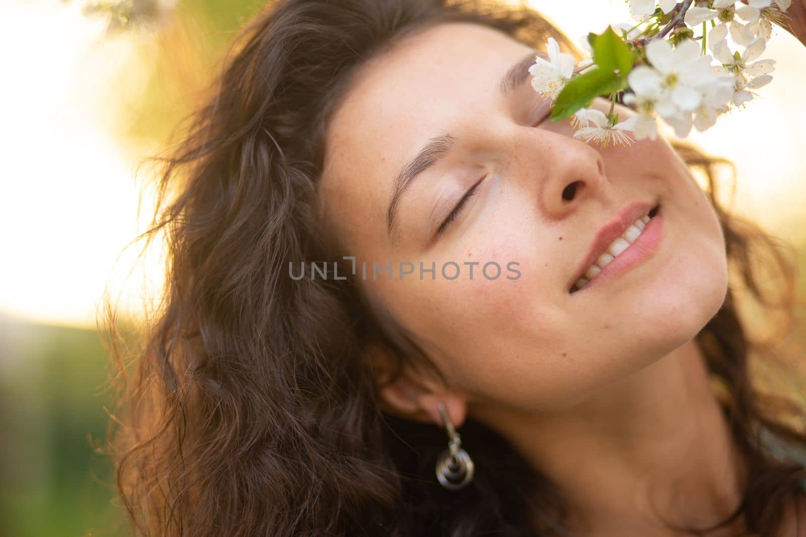 A young brunette girl poses with a blossoming cherry branch.