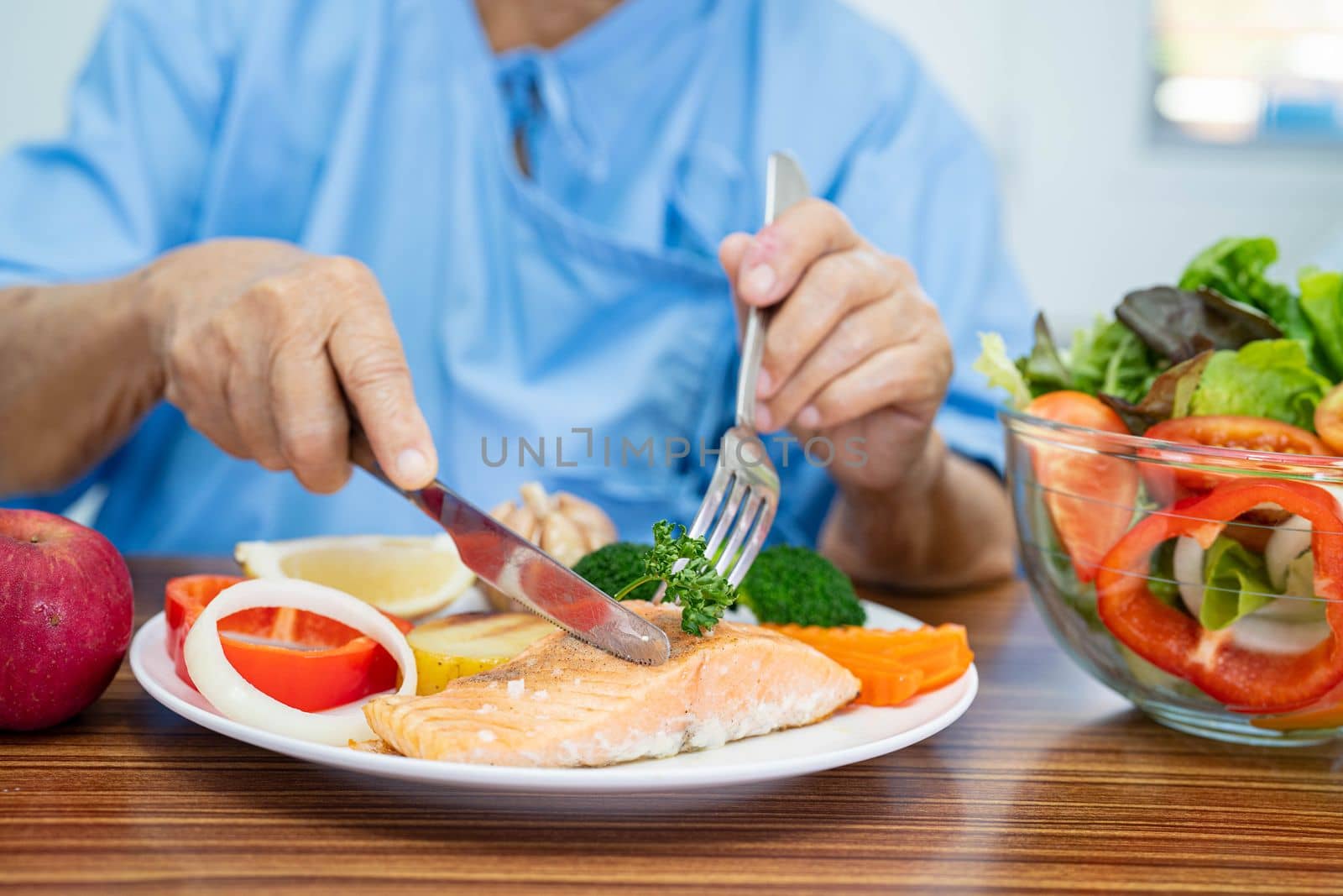 Asian senior or elderly old lady woman patient eating Salmon steak breakfast with vegetable healthy food while sitting and hungry on bed in hospital. by pamai