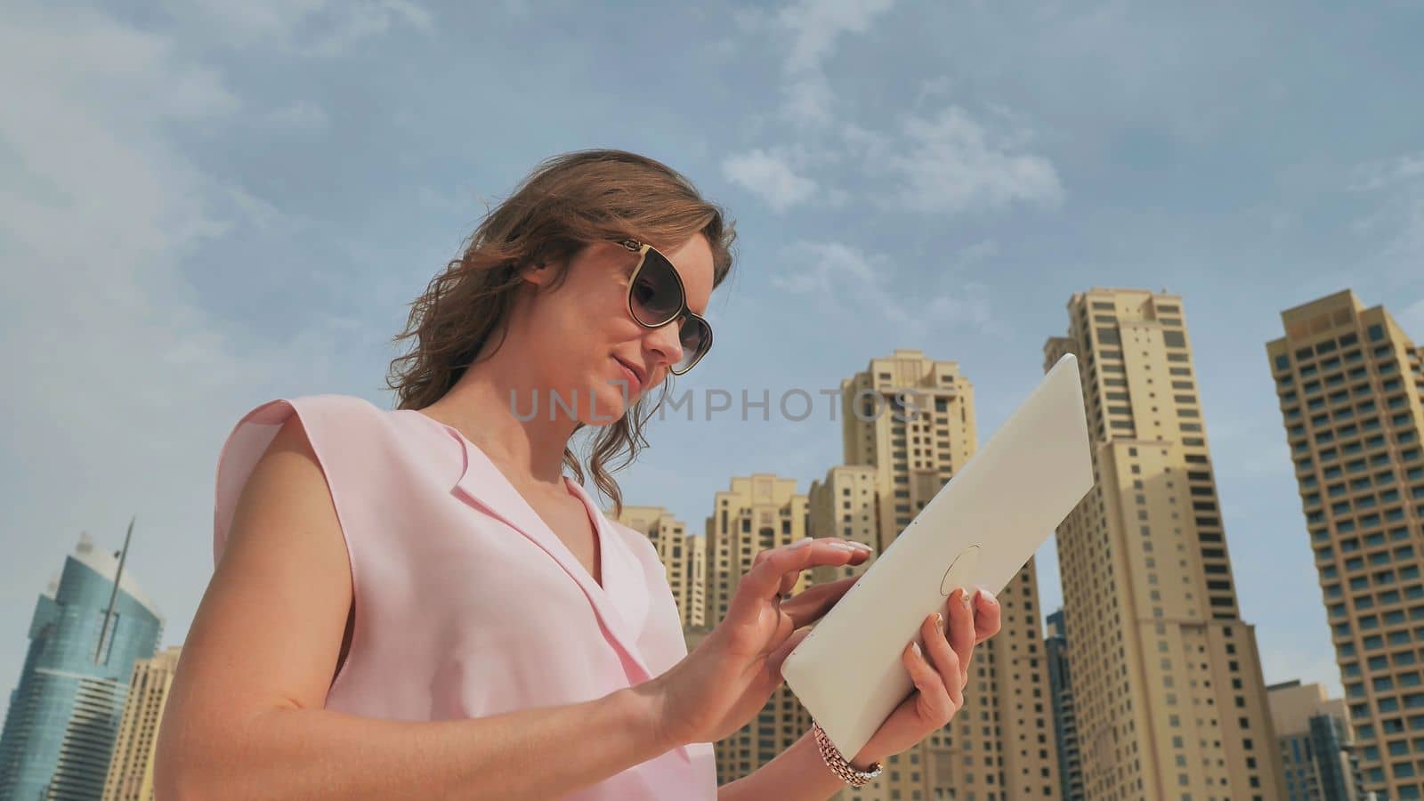 A girl works on a tablet against the background of skyscrapers of a metropolis