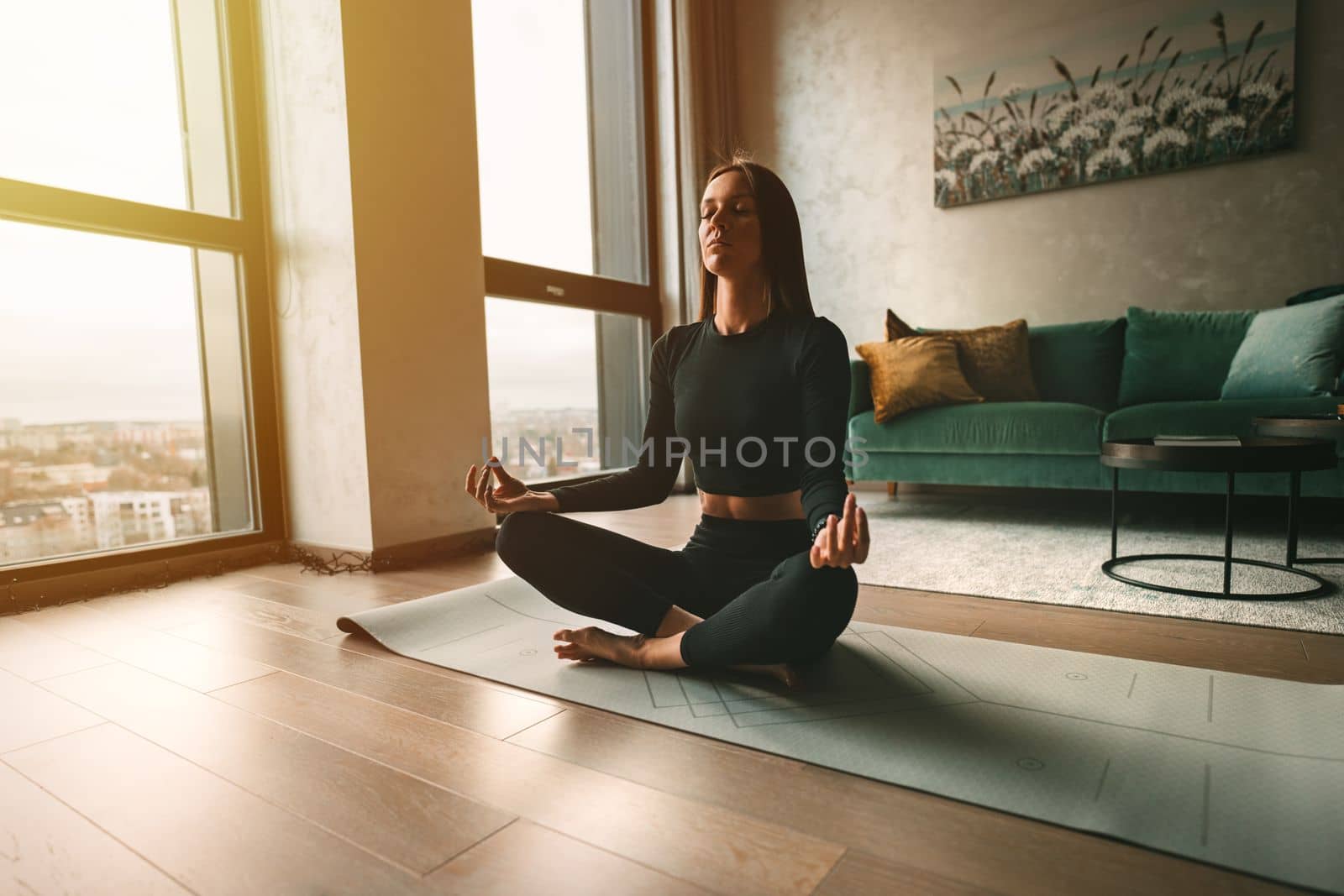 Woman practices yoga and meditates with eyes closed at home. Calmness and appeasement concept. Woman sitting in easy pose or sukhasana with mudra. by DariaKulkova