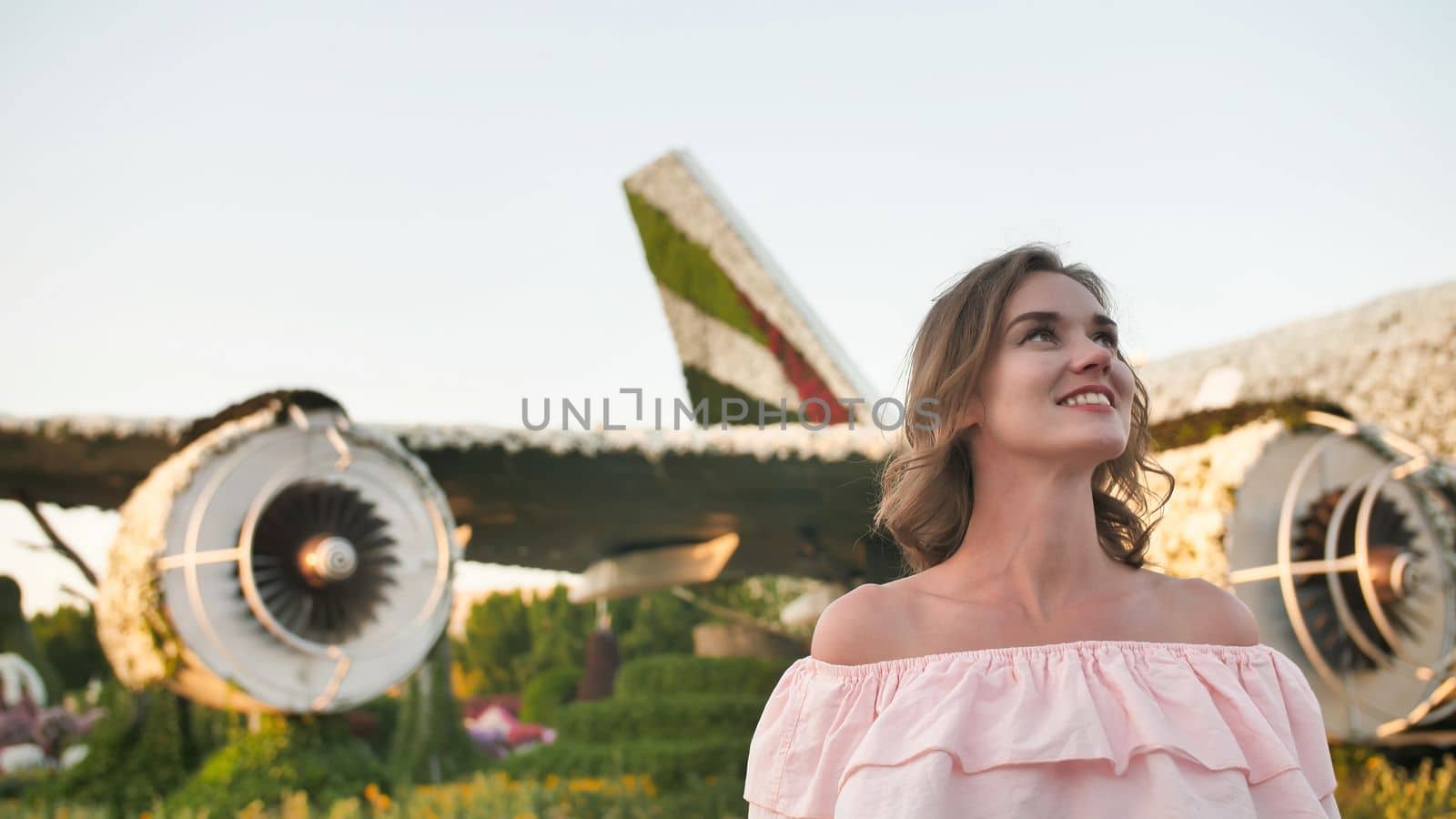 A girl admires in a city park on the background of an airplane of flowers