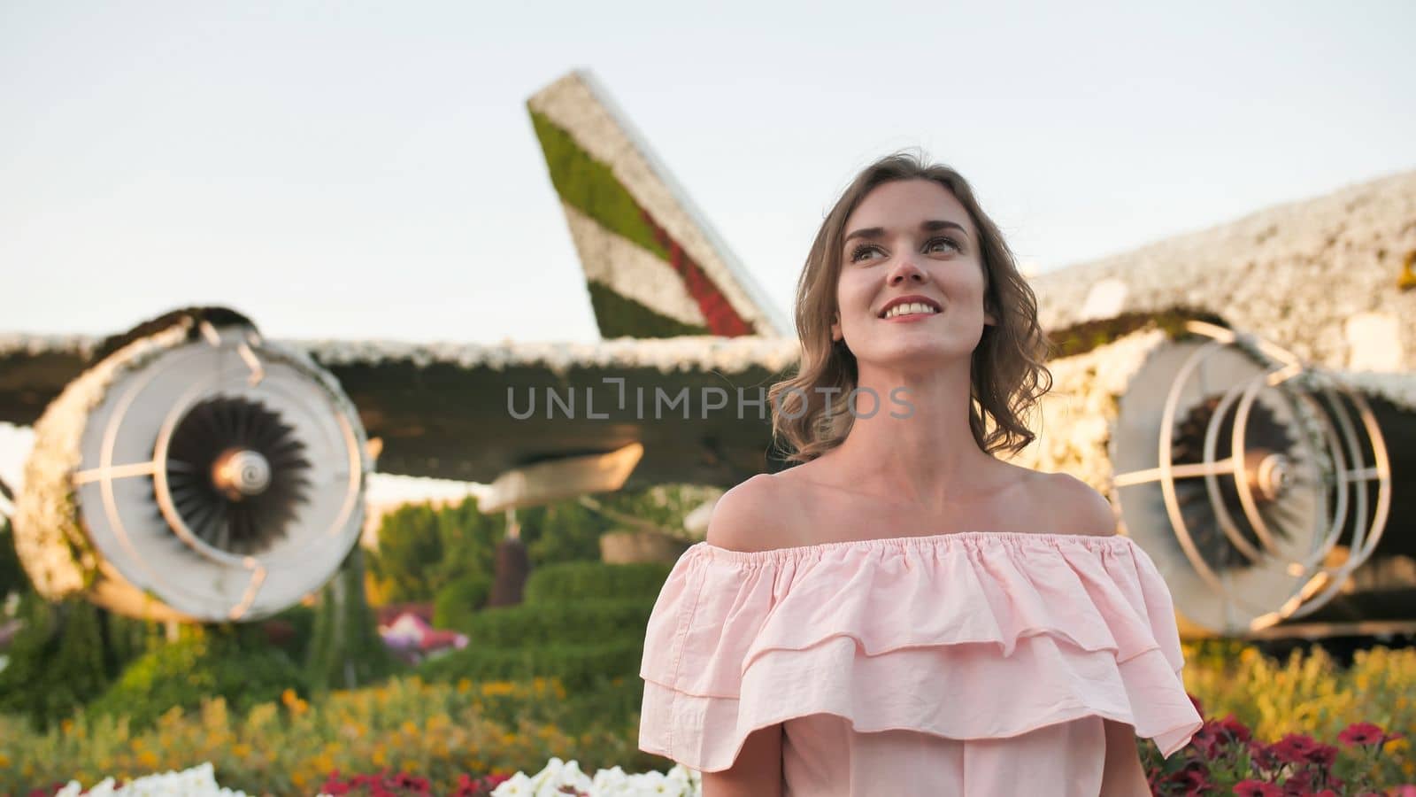 A girl admires in a city park on the background of an airplane of flowers