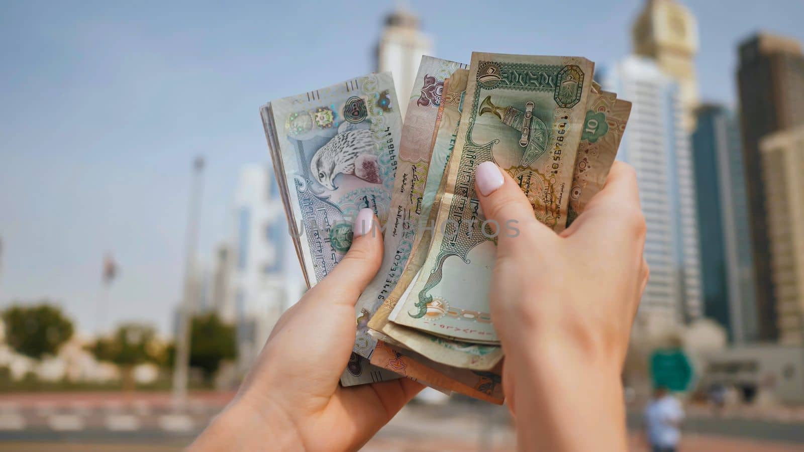 The girl holds in her hands the money of the United Arab Emirates on the background of the city center of Dubai