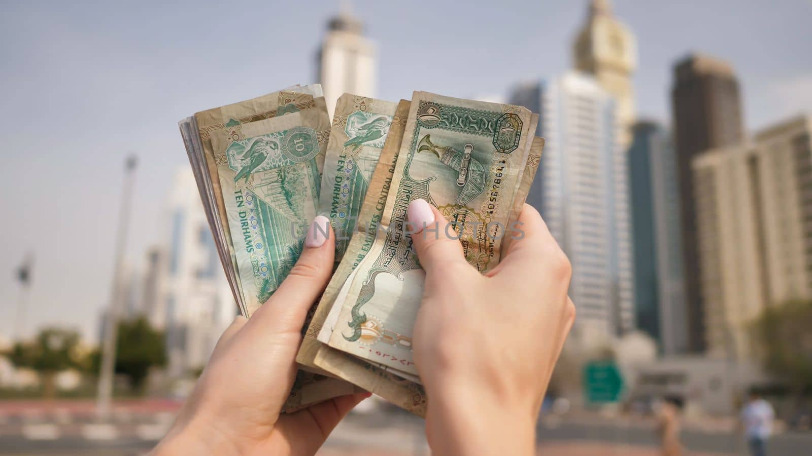 Hands of a girl holding money of the United Arab Emirates on the background of Dubai skyscrapers