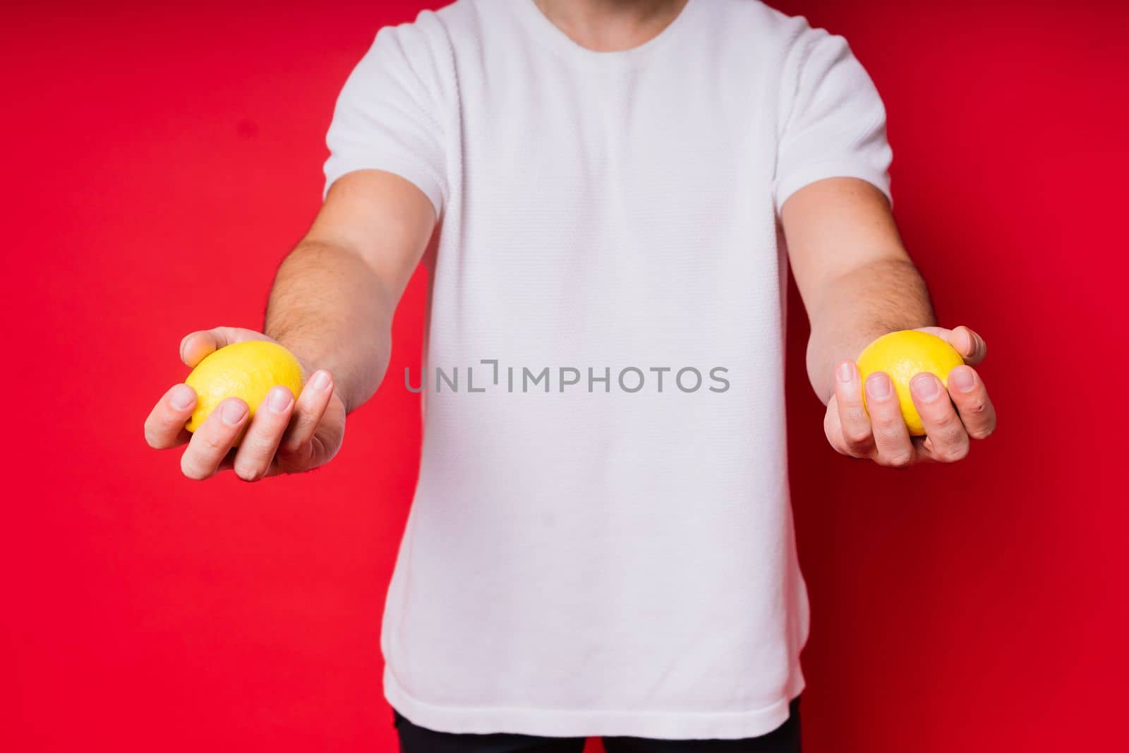 Portrait of young bearded man holding lemons in both hands on isolated red background by Zelenin