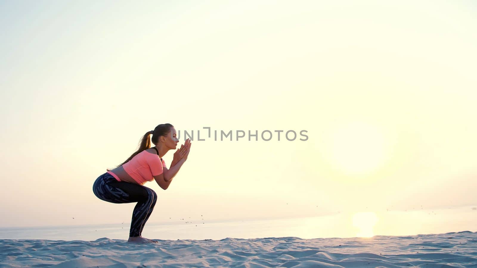 Healthy, young beautiful woman meditating, stretching, practicing yoga on the sea beach, at sunrise, Makes exercises for balance and coordination, deep muscle tone. High quality photo
