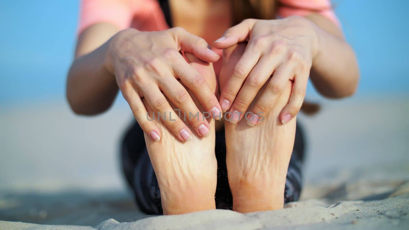 Beautiful blond woman doing stretching exercises on the beach. Close-up of foot. High quality photo