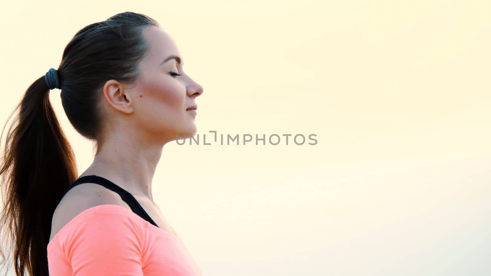 Healthy, young beautiful woman meditating, practicing yoga among the sand, on the beach, by the sea, river, at dawn, at sunrise, closeup.