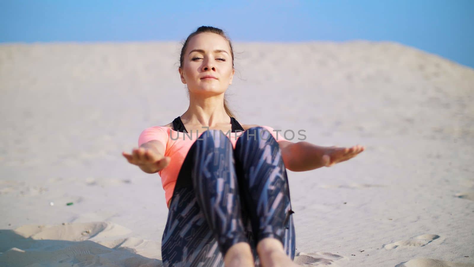 Healthy, young beautiful woman performs exercises for muscles of the press, picks up the body, legs, pumps the press lying on the sand, on the beach, at sunrise. High quality photo