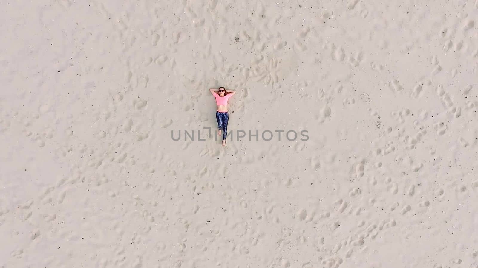 Stylish young athletic beautiful woman in sunglasses, lying on the sand, on a deserted beach, in summer. View from above, aero video. by djtreneryay