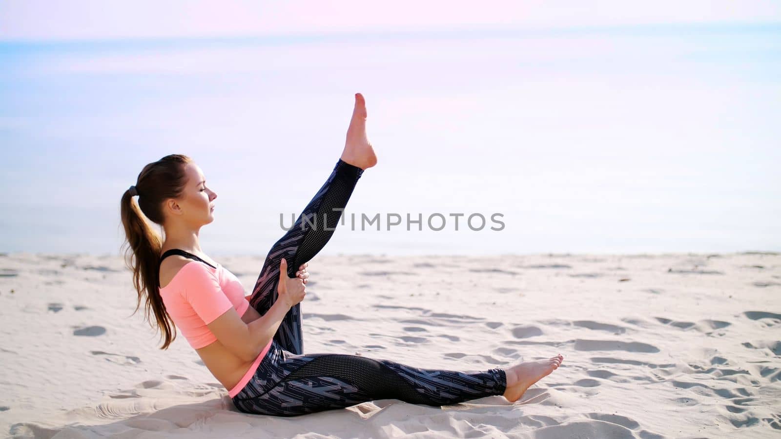 Healthy, young beautiful woman performs exercises for muscles of the press, picks up the body, legs, pumps the press lying on the sand, on the beach, at sunrise by djtreneryay