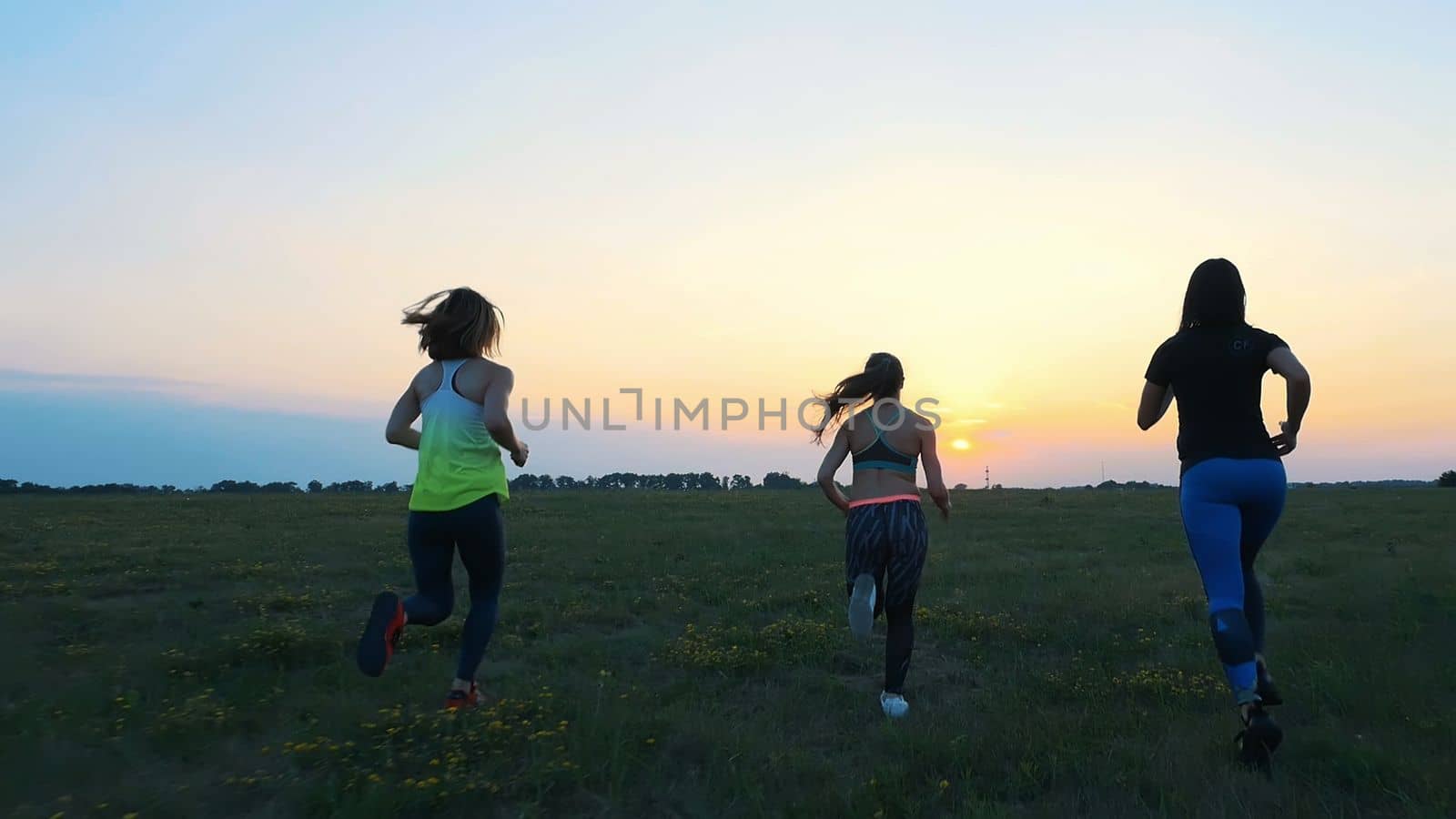 Beautiful, athletic, young women in sunglasses, in tights,, run synchronously along the green meadow, field. In summer, jogging, sunset,. High quality photo