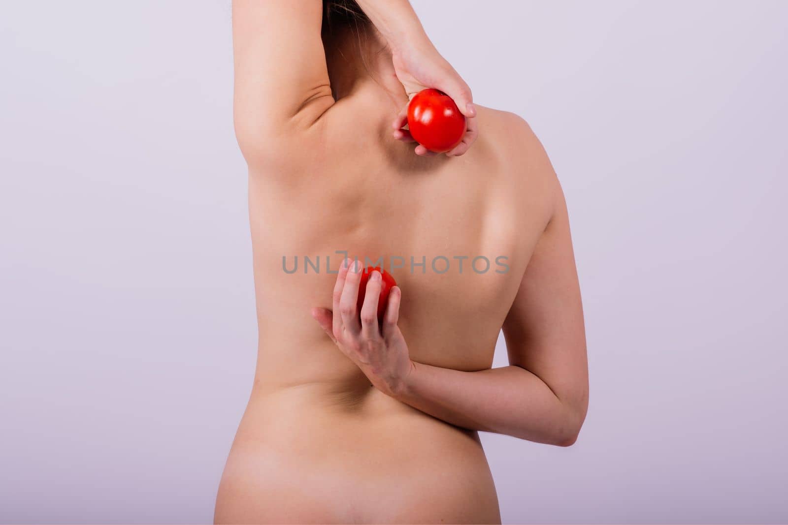 Healthy young woman holding a tomatos over her eyes, laughing, bare shoulders, topless.