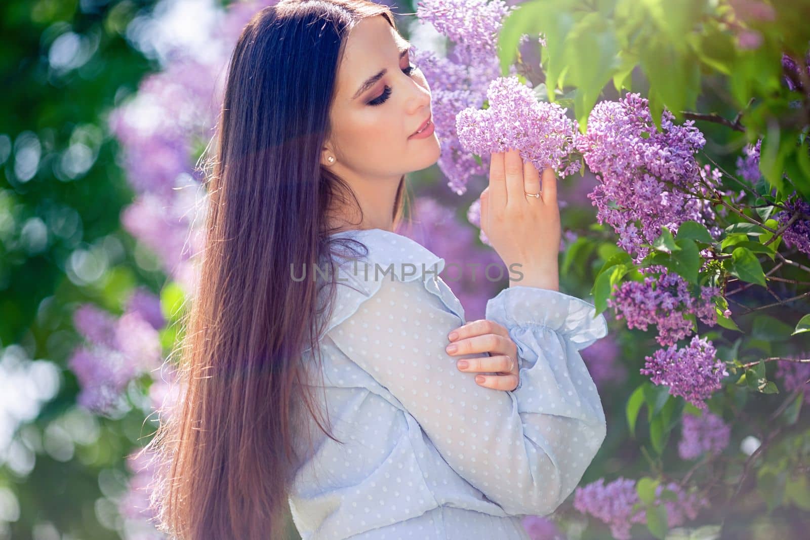 Beautiful brunette girl, with long hair, standing near blossom lilac tree in the summer in the park, sunny day. Close up