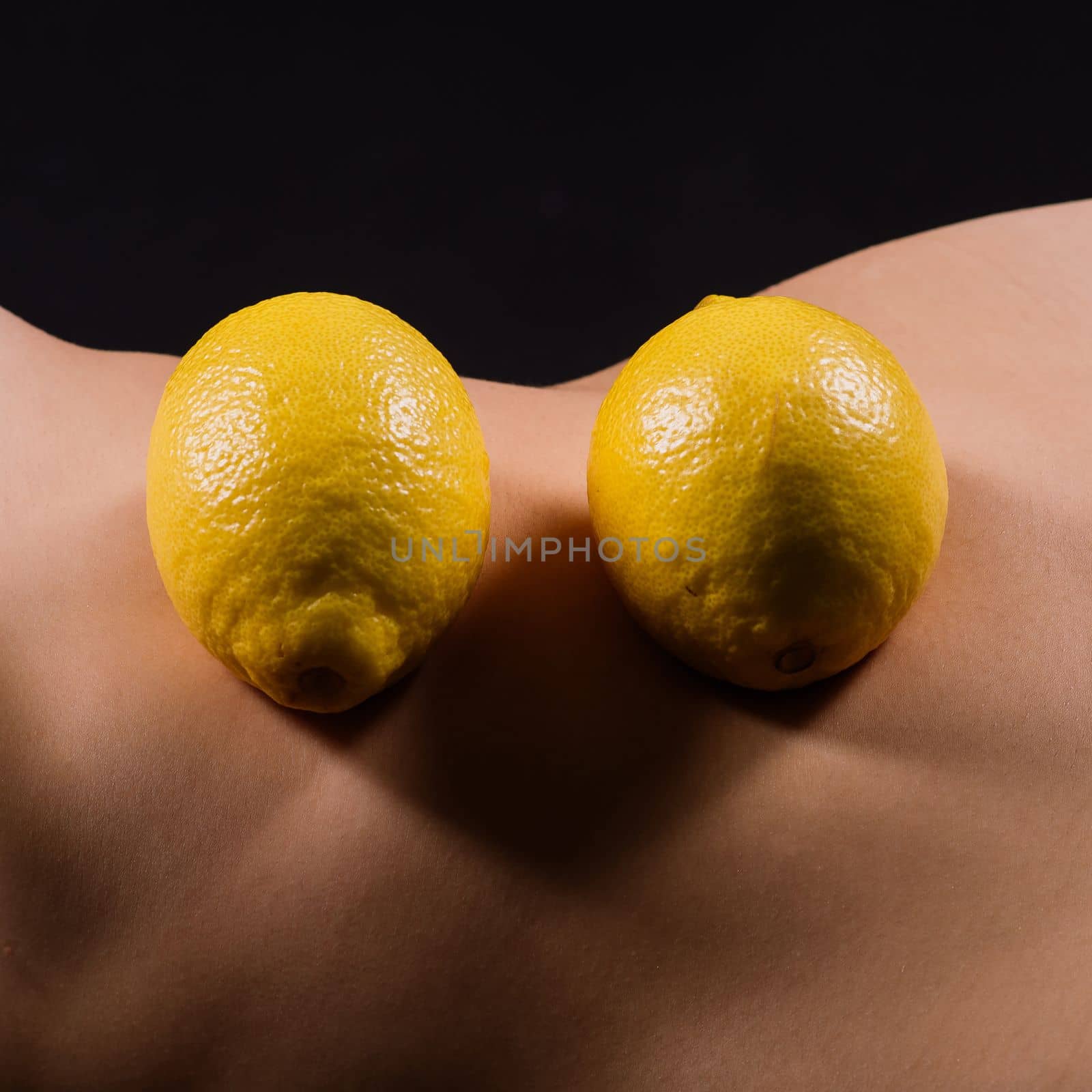 Young woman with cellulite problem and lemon on a dark background, closeup