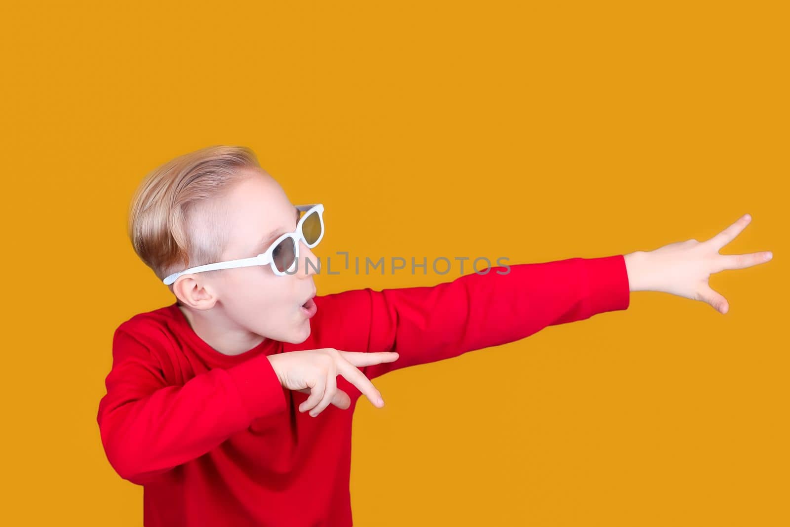a cool child on a yellow background and in children's 3D glasses shows the direction to the side with his hands