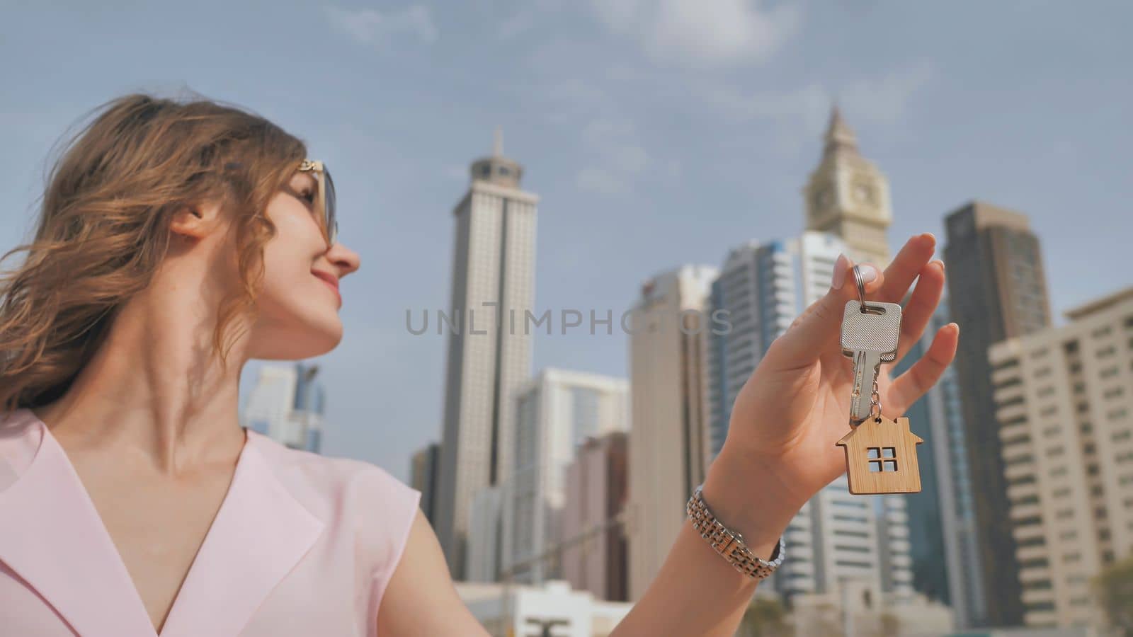 The concept of buying an apartment. Girl holds the keys to a new house against the backdrop of skyscrapers in the city