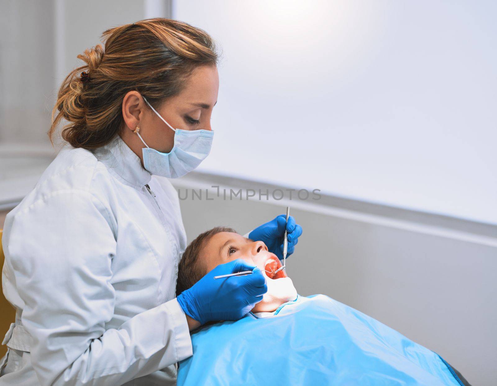 Just this last bit and we are done. a young little boy lying down on a dentist chair while getting a checkup from the dentist. by YuriArcurs