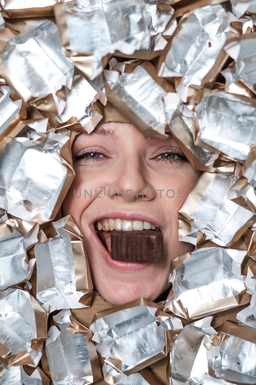 The face of a Caucasian woman surrounded by candy wrappers. The girl eats a bar of chocolate. by mrwed54