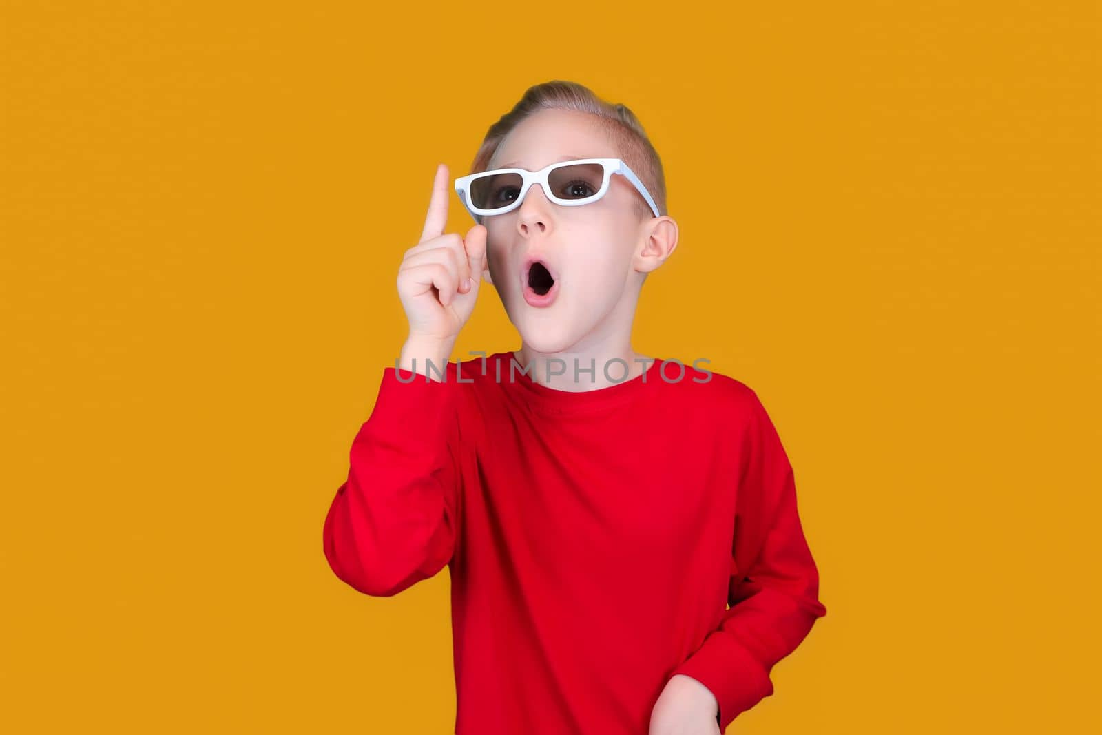 a child in children's 3D glasses raised his finger up on a yellow background