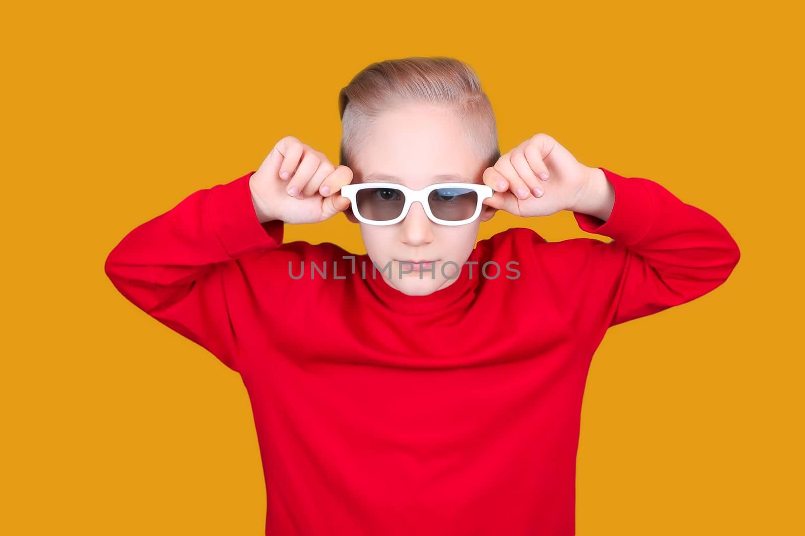 a child in a red jacket holds his hands behind his glasses on a yellow background