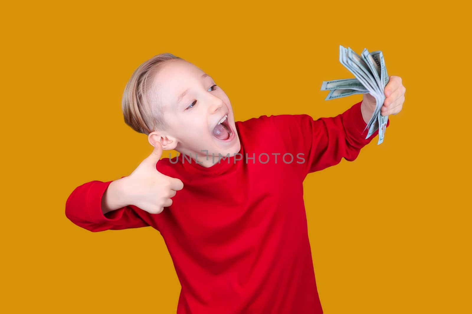 happy child holds banknotes in his hand and gives a thumbs up