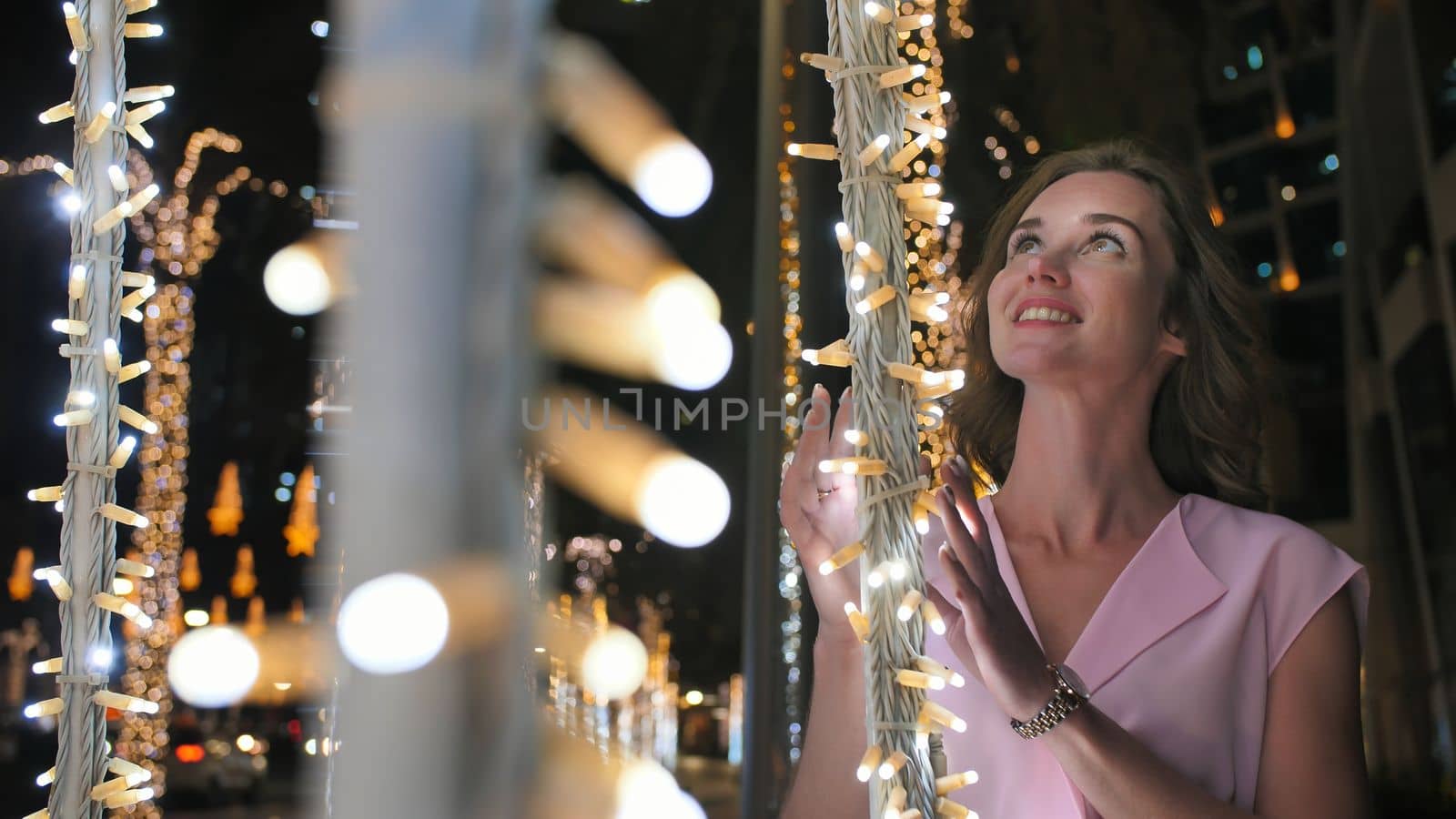 The girl gently touches the glowing lights on a palm tree in the night city of Dubai