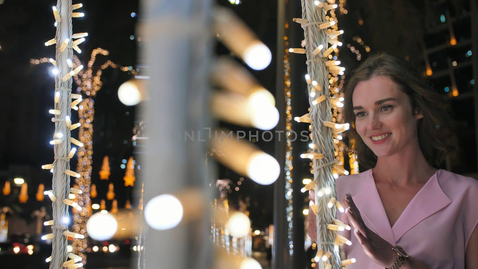 The girl gently touches the glowing lights on a palm tree in the night city of Dubai