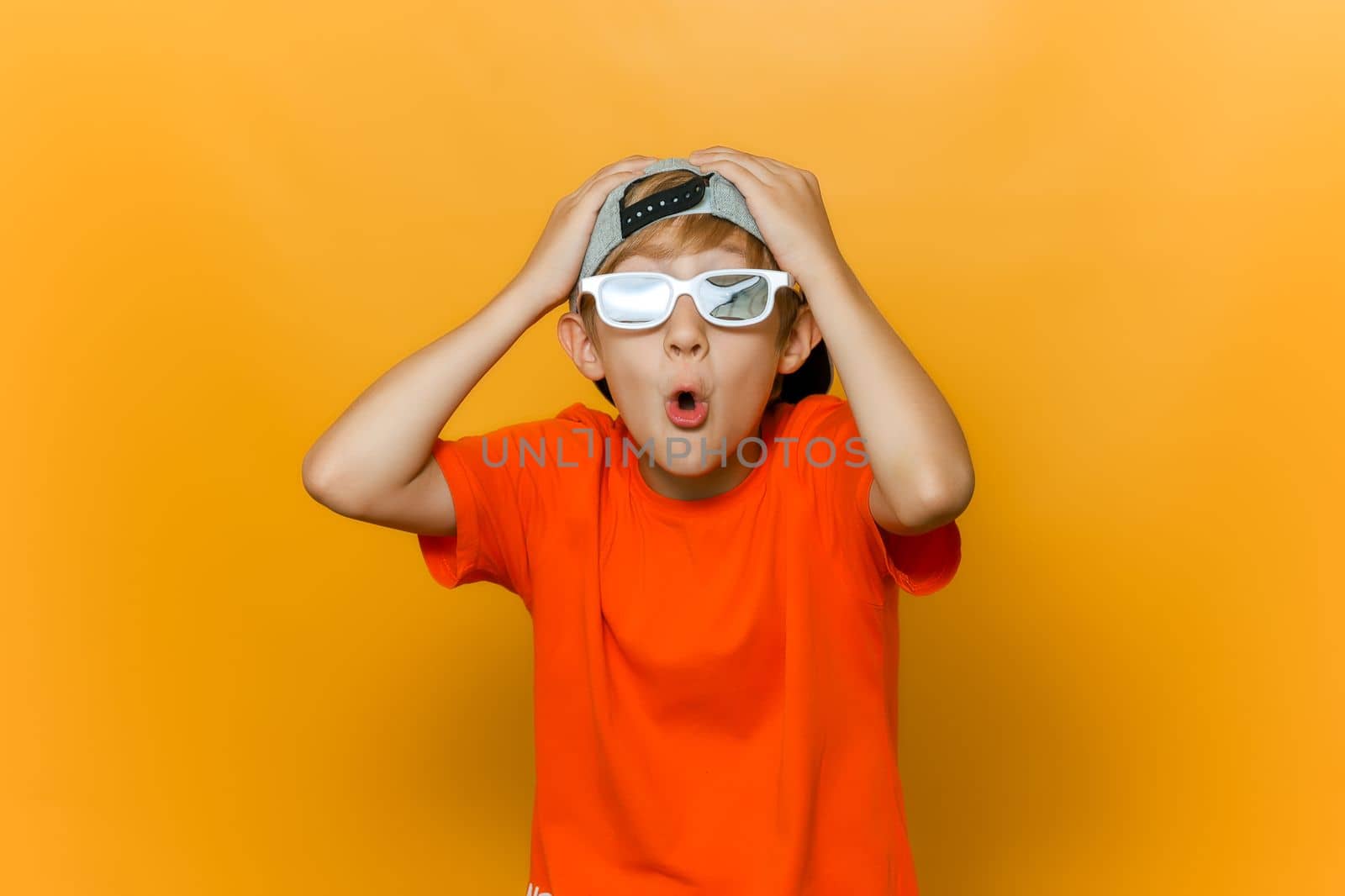 a child in a cap and glasses for watching movies grabbed his head with both hands and twisted his lips into a tube and shows emotions of surprise by RomanChoknadii