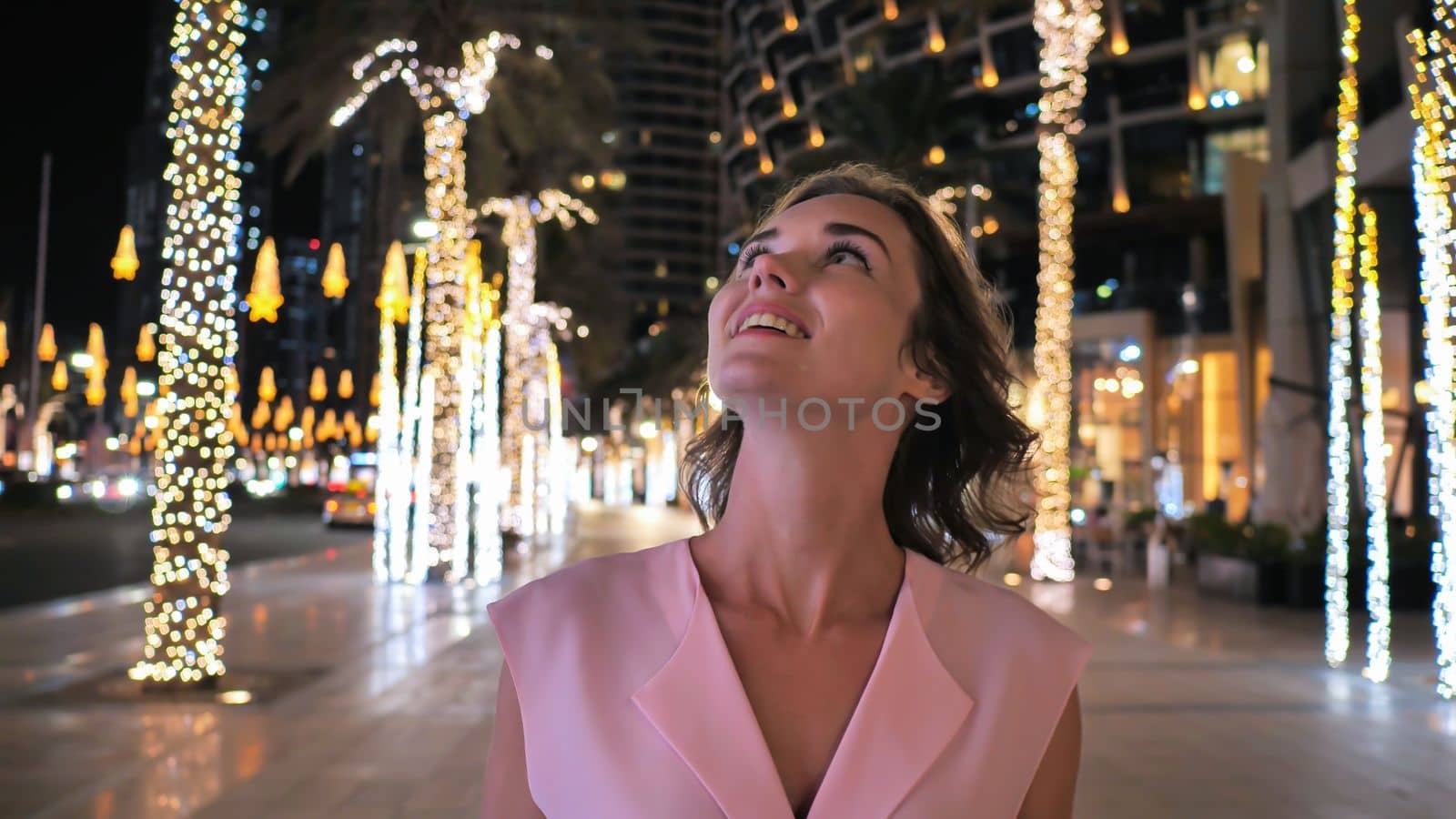 The girl gently touches the glowing lights on a palm tree in the night city of Dubai