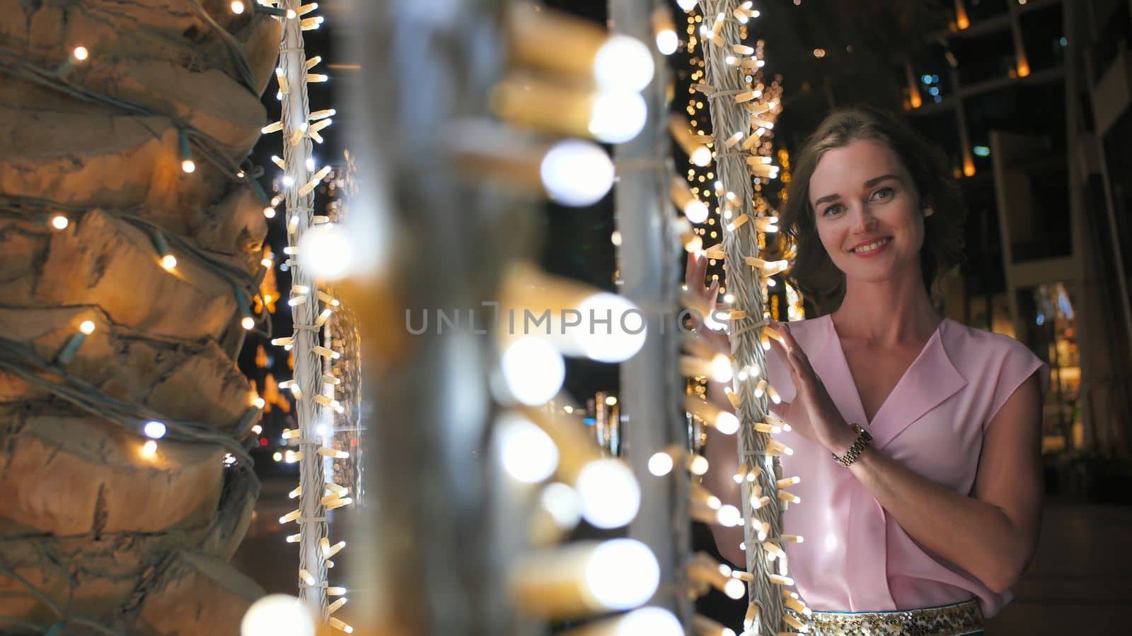 The girl gently touches the glowing lights on a palm tree in the night city of Dubai