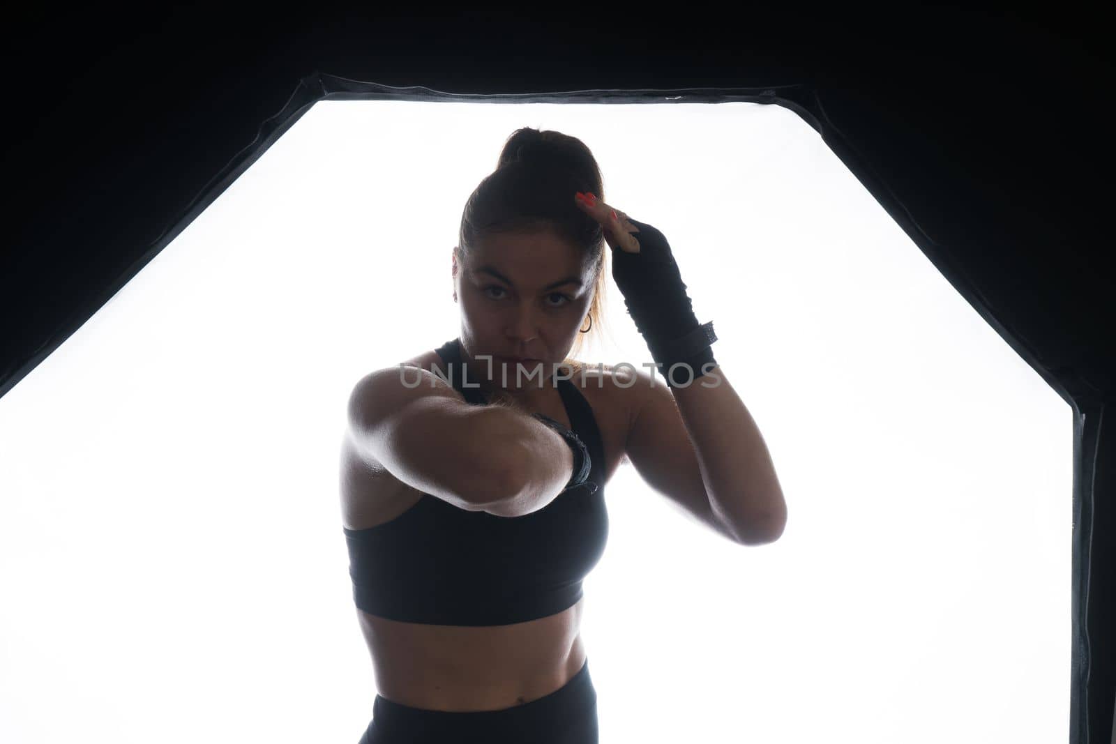 Strong sportswoman in boxing gloves prepared high kick. Isolated on a white, red, yellow background