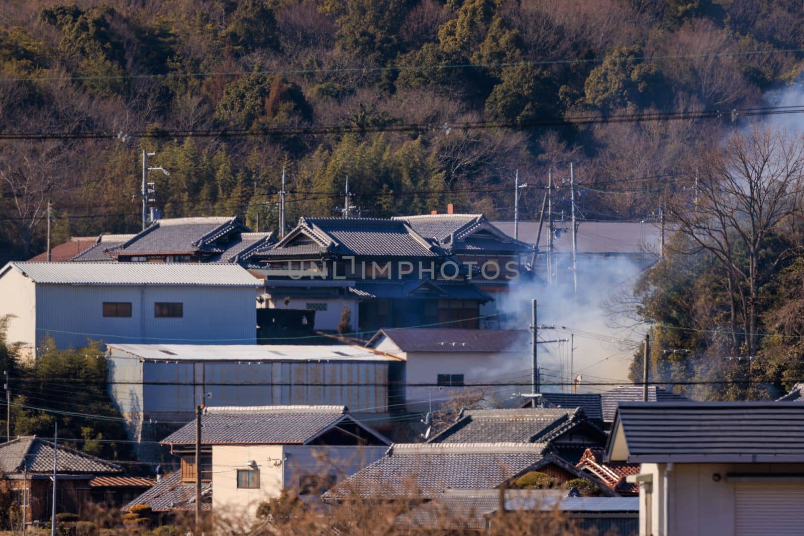 Smoke rises from houses in suburban Japanese neighborhood on sunny day by Osaze