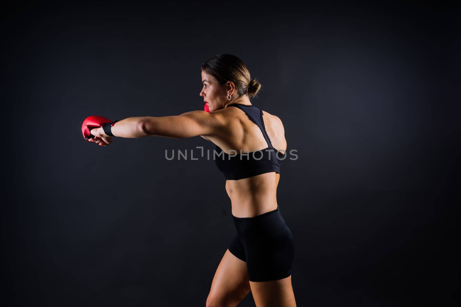 Strong sportswoman in boxing gloves prepared high kick. Isolated on a white, red, yellow background