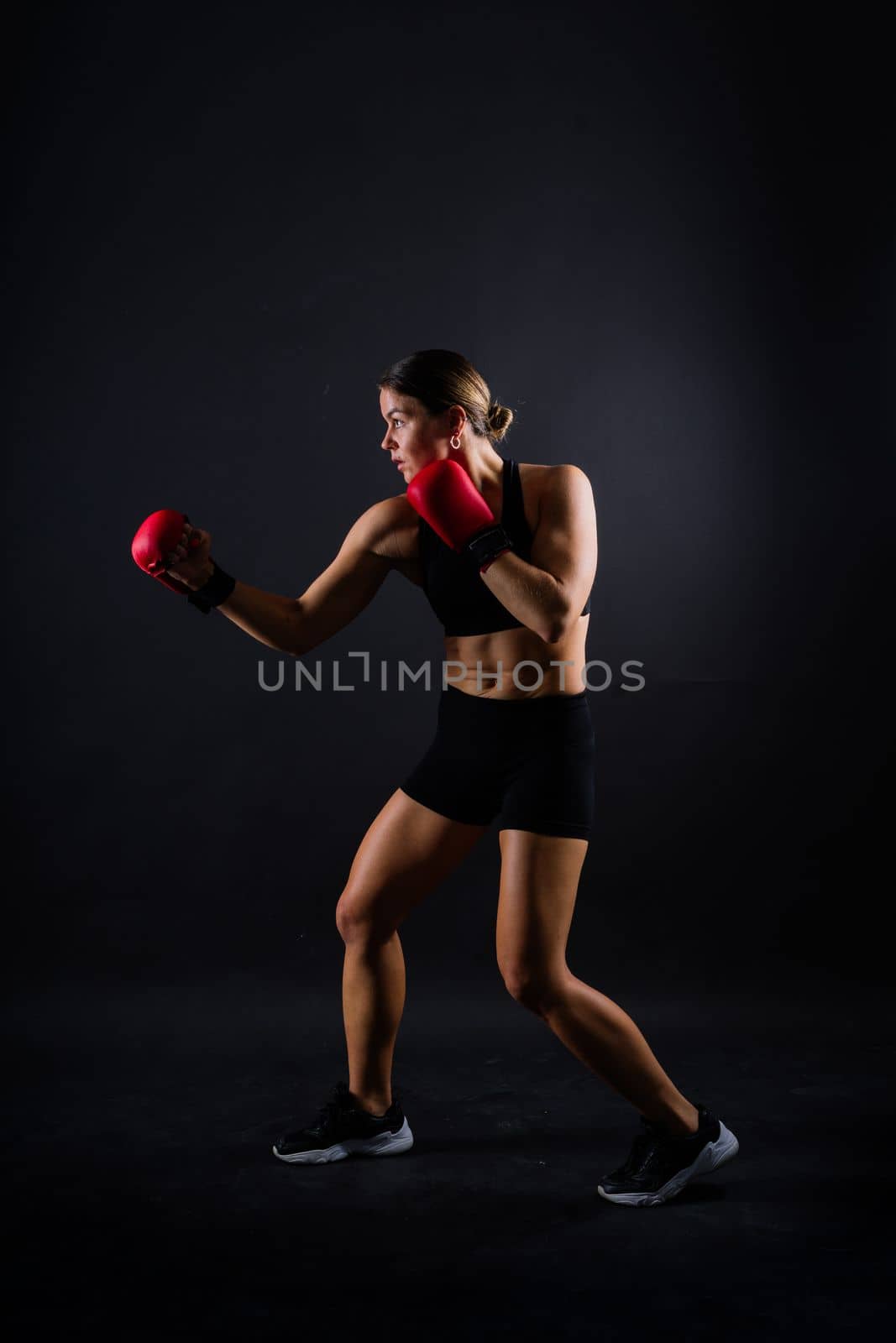Strong sportswoman in boxing gloves prepared high kick. Isolated on white, red, yellow background by Zelenin
