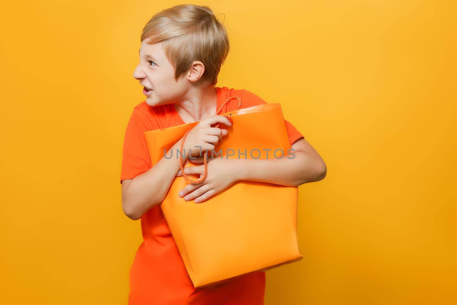 a boy in an orange T-shirt holds a package with both hands clutching it to his chest and is angry