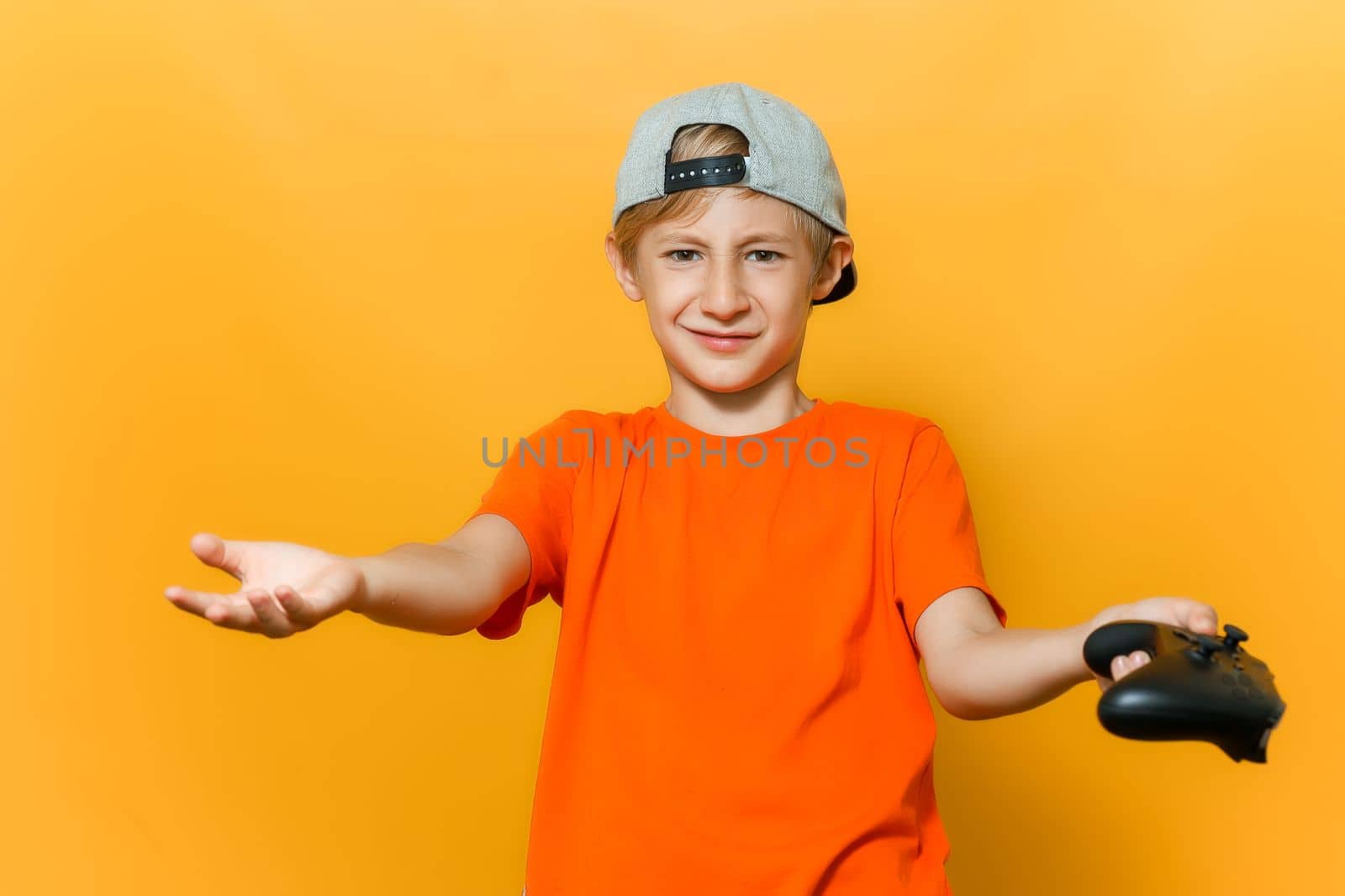 a boy in a cap and an orange T-shirt spread his hands in different directions he holds a gamepad in one hand