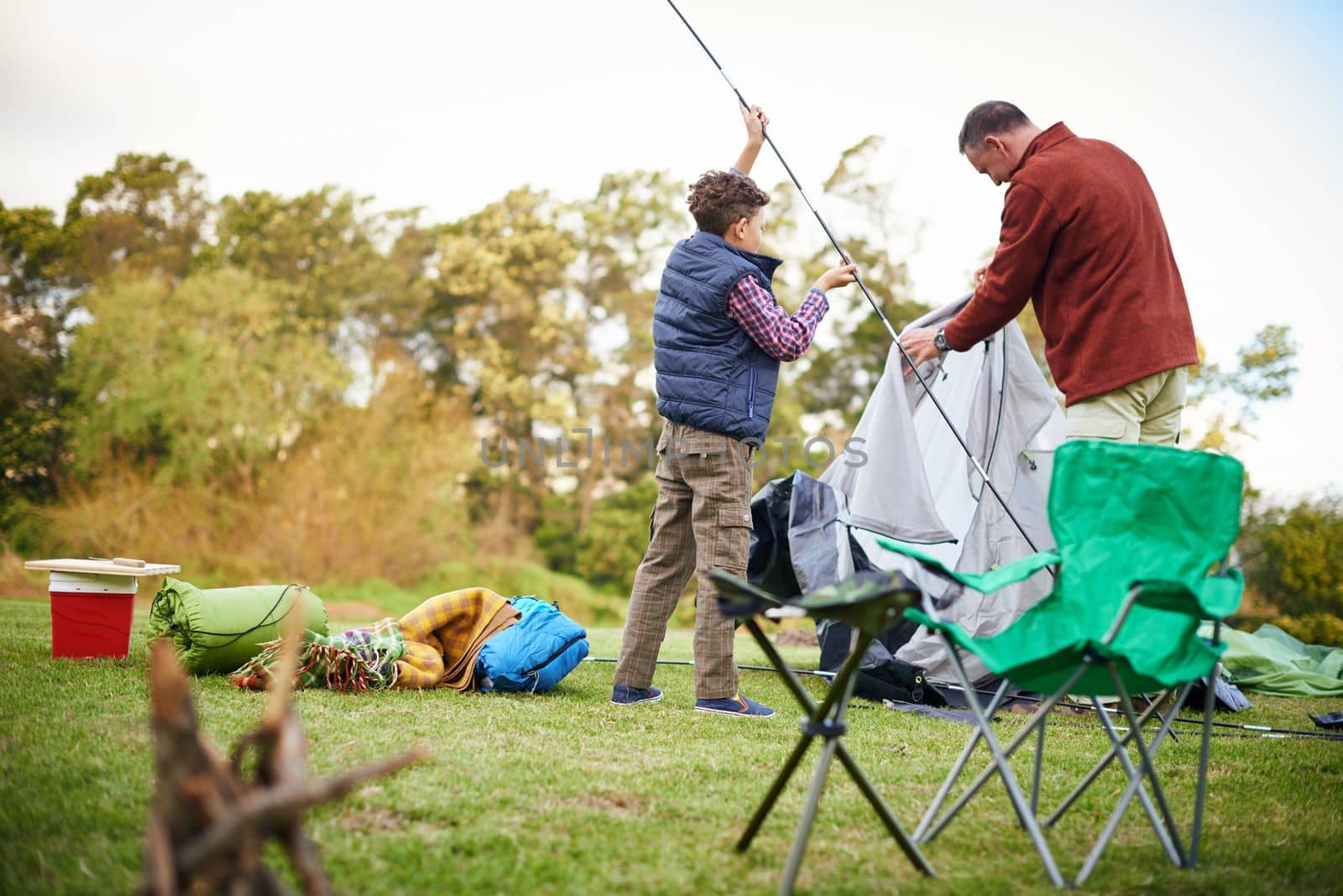 Its a boys only camping trip. a father and son setting up a tent together while camping. by YuriArcurs
