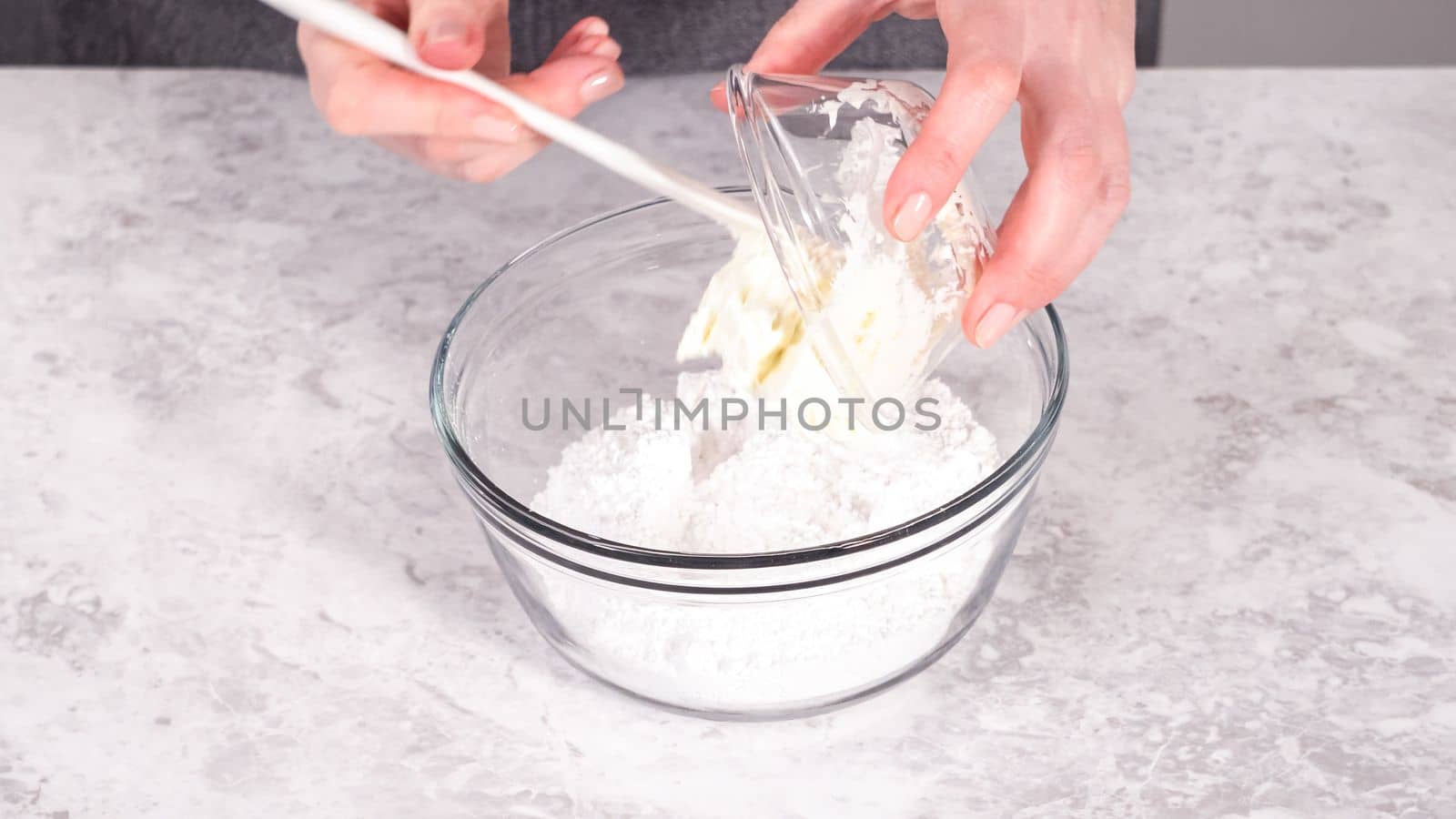 Step by step. Mixing ingredients in a glass mixing bowl to prepare cream cheese frosting.