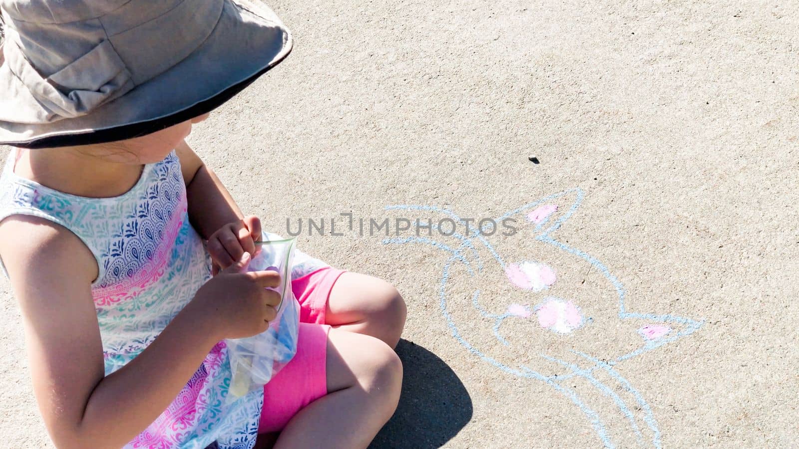 Little girl drawing with chalk on a sidewalk on the summer day.