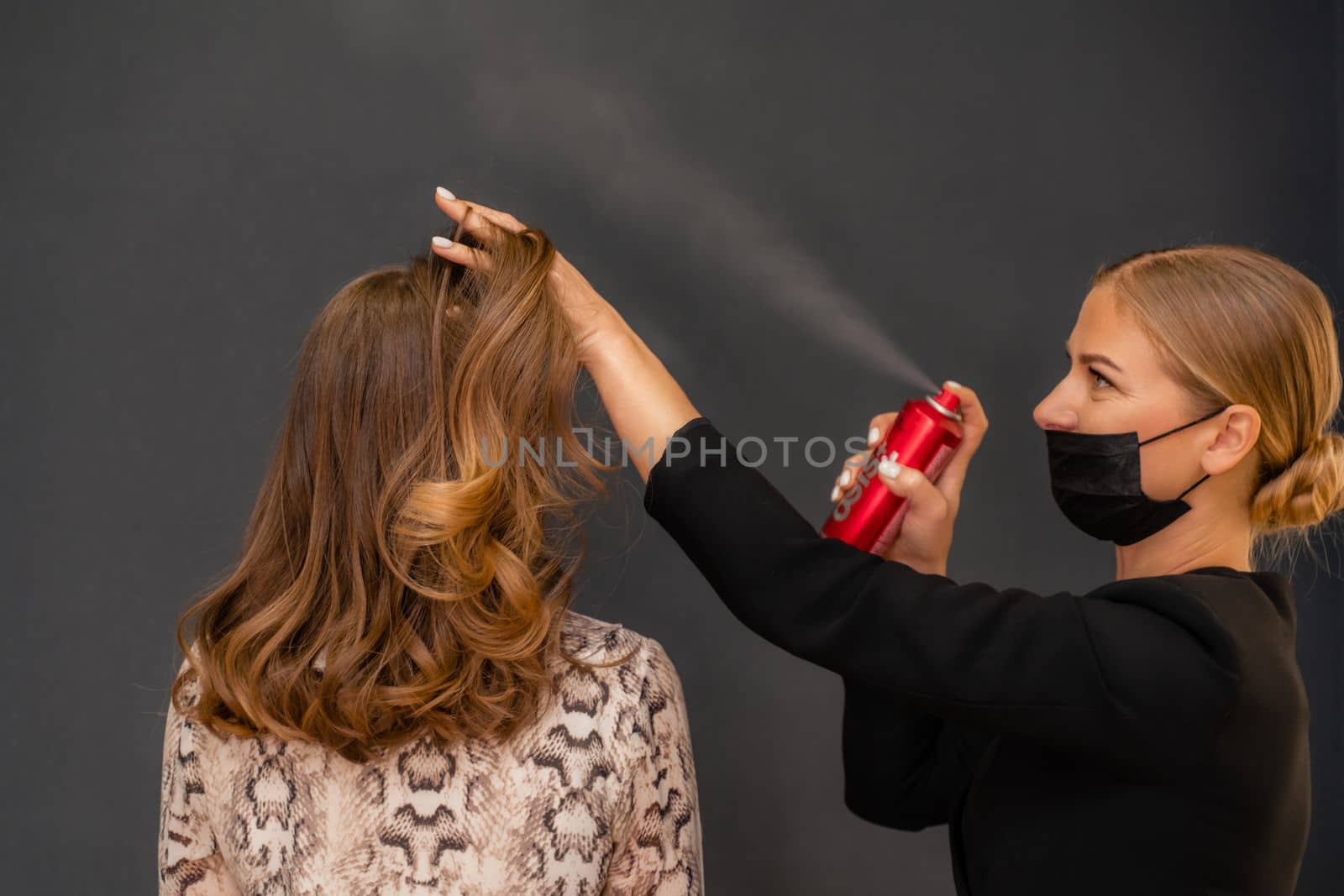 Women salon hairstyle. Hairdresser uses hairspray on client's hair in salon, Portrait of two beautiful women.