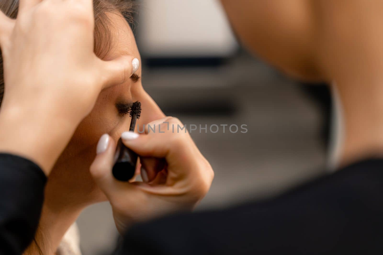 Makeup artist paints eyelashes to a woman in a beauty salon. by Matiunina