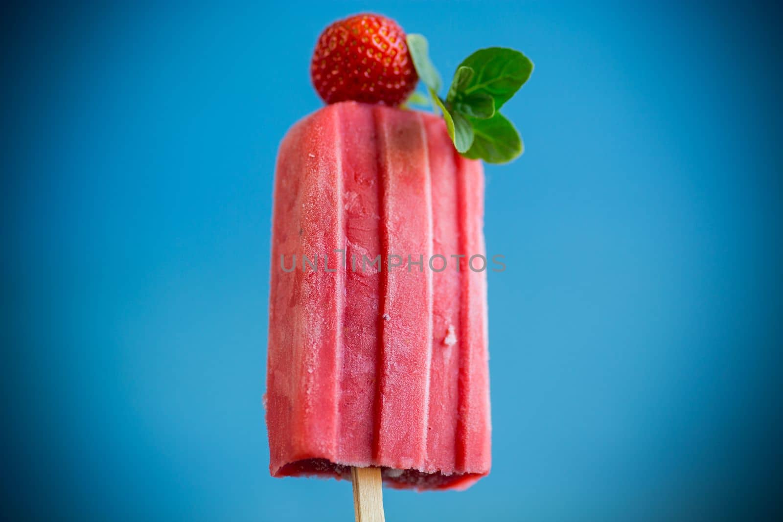 cooked homemade strawberry ice cream on a stick, isolated on blue background