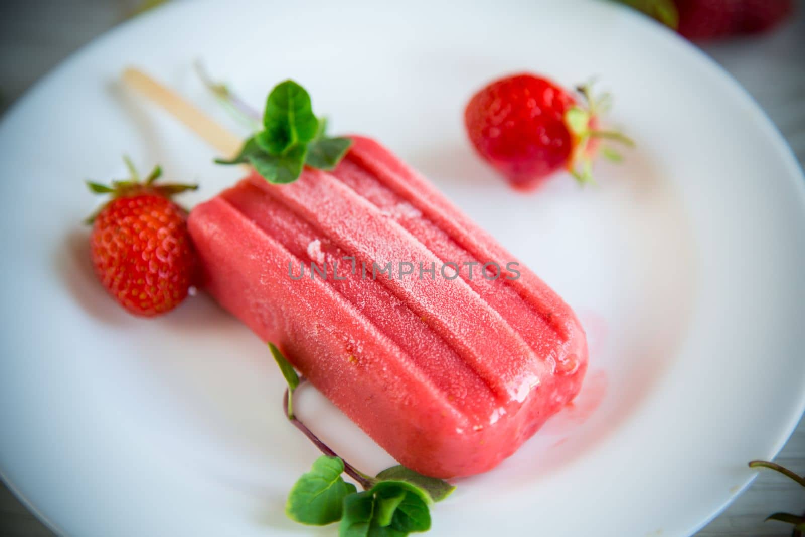 cooked homemade strawberry ice cream on a stick in a plate with strawberries