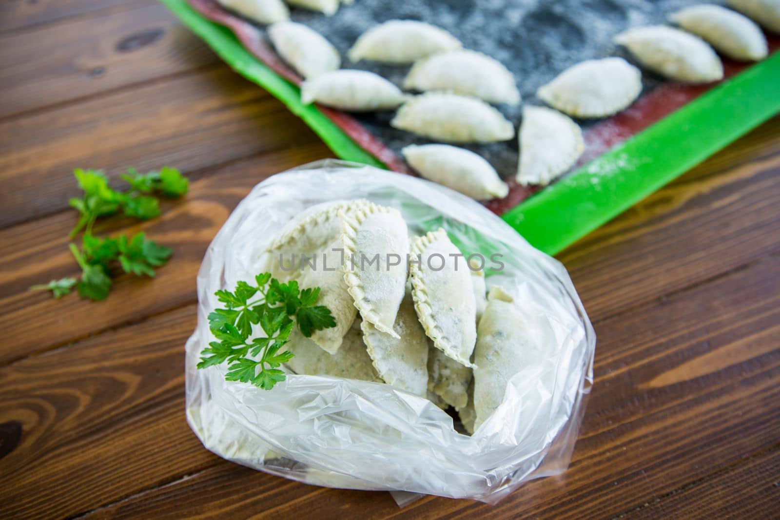 Raw green dough dumplings with parsley, dill. Raw dumplings in a bag on a wooden table.