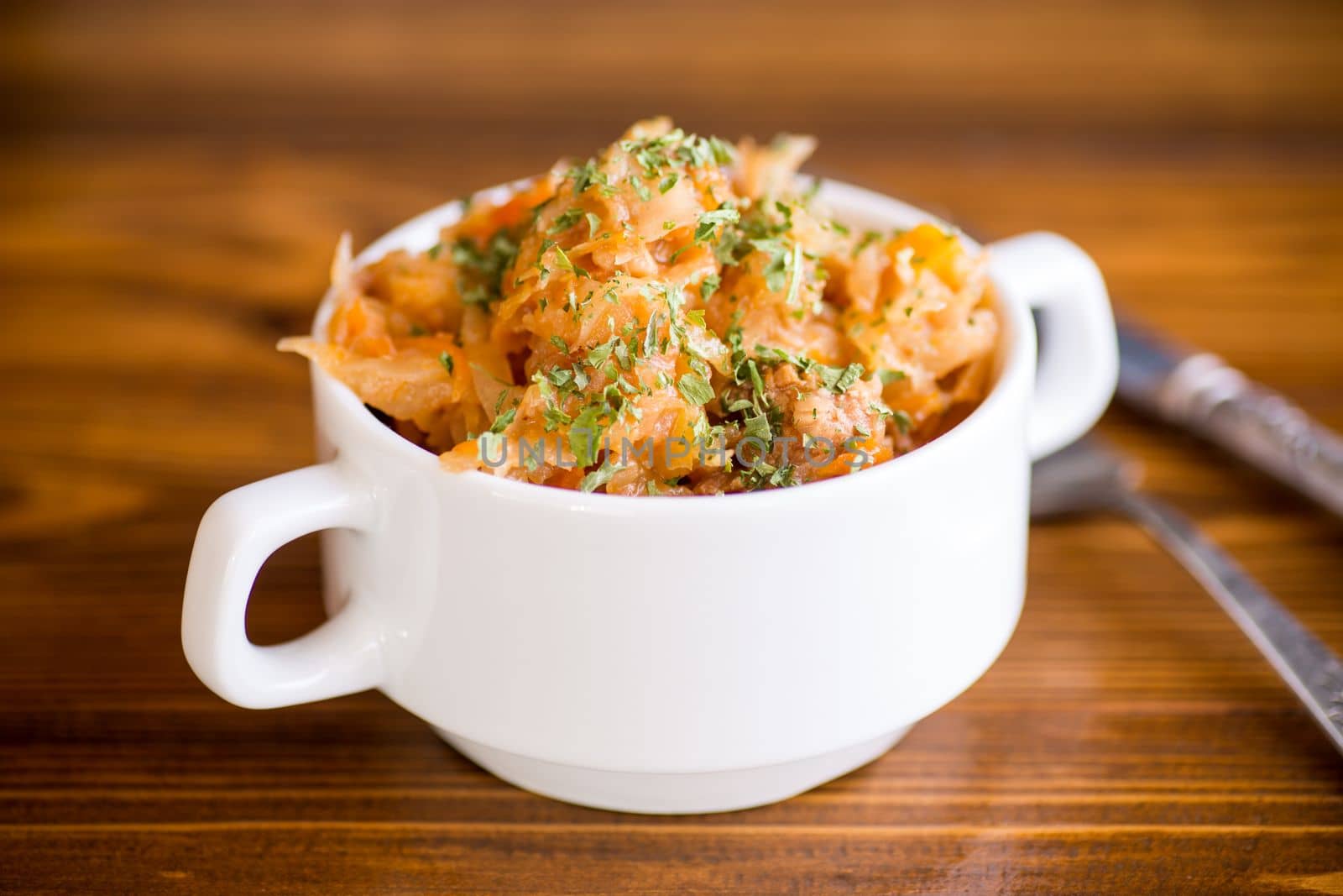 stewed cabbage with carrots and spices in a bowl on a wooden table.